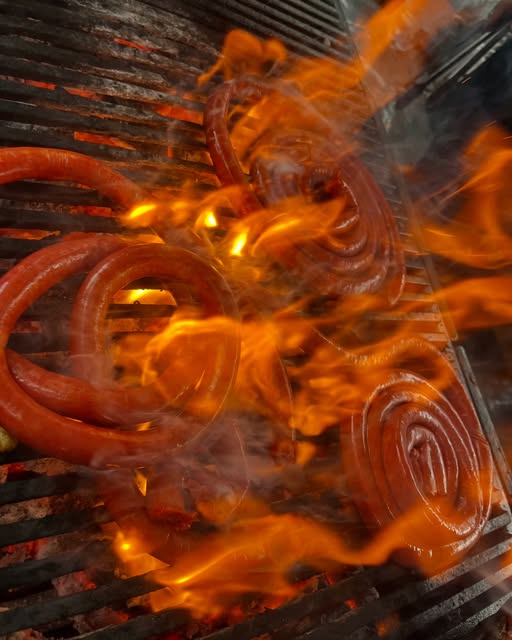 Chorizos rojos asándose entre llamas en la parrilla de La Paloma Choncha
